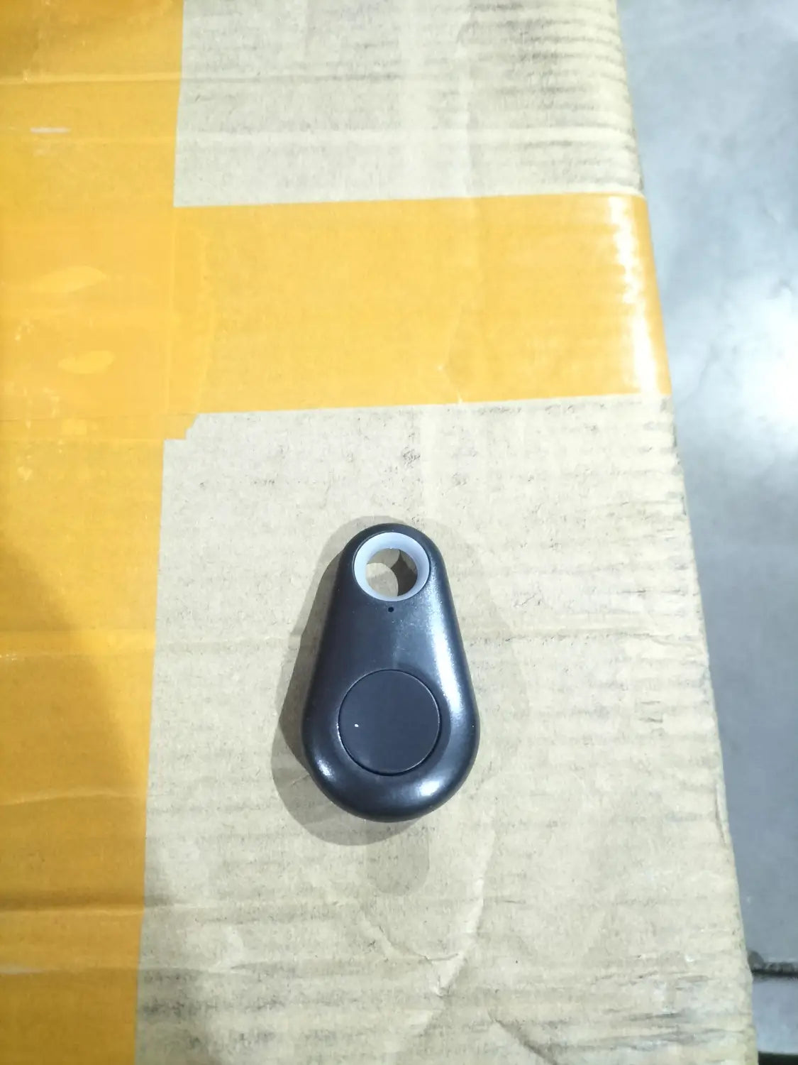 Black sleek teardrop shaped anti lost object bluetooth tracker with a circular button and attachment hole designed as a water drop lost object finder.