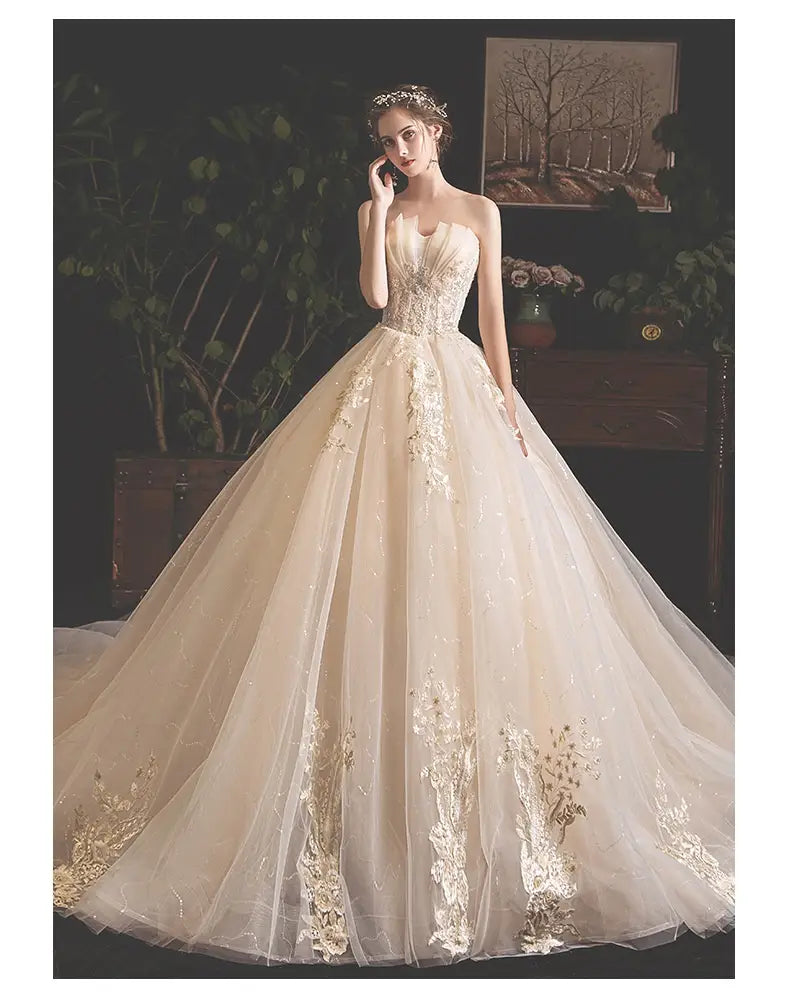 A strapless ivory bride summer tube top wedding gown featuring intricate gold lace appliqués and a mori style trailing voluminous tulle skirt.