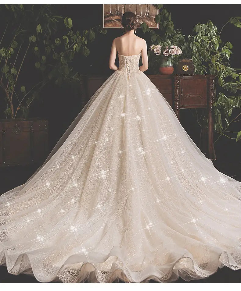 A flowing ivory bride summer tube gown featuring a structured bodice and a mori style trailing skirt with a glittering tulle overlay and delicate lace trim.