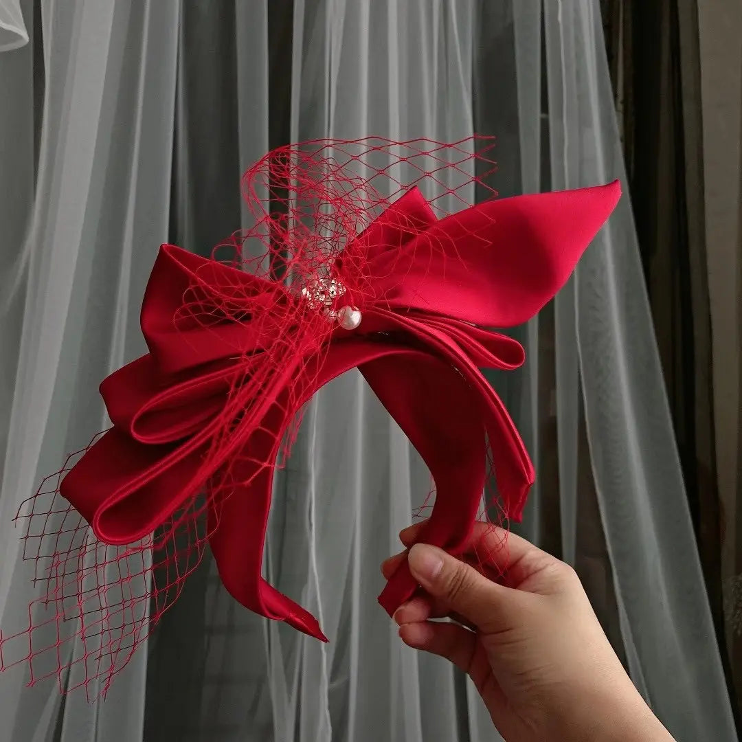 A vibrant red satin wedding satin headband featuring a bow adorned with delicate mesh and a pearl accent for fashion bridal wedding occasions.