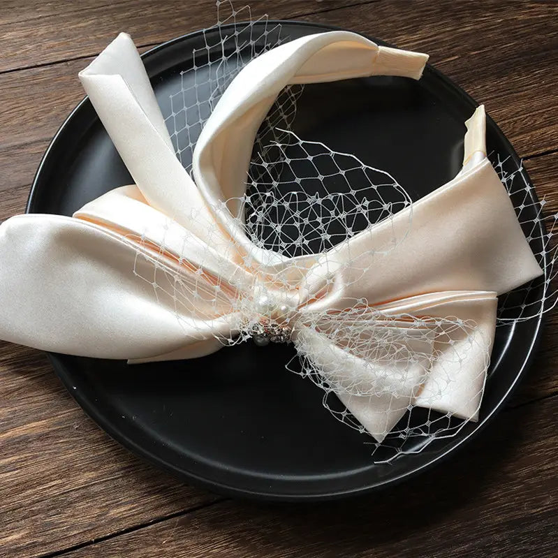 Red bow fashion bridal wedding satin headband featuring a cream satin bow with delicate white lace and a pearl-adorned center elegantly displayed on a black plate.