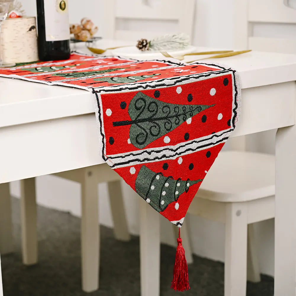 red woven christmas table runner with green christmas tree patterns black and white polka dots and a matching red tassel perfect for festive christmas table decor