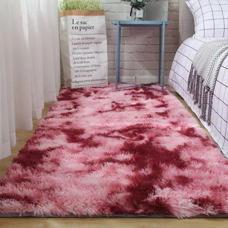 A plush carpet floor mat featuring a shaggy texture with a gradient of pink and deep red hues designed for comfortable indoor use.