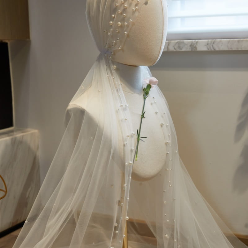 A delicate white sheer super fairy long bridal hijab veil adorned with a row of small pearls along its edge elegantly draped over a mannequin.