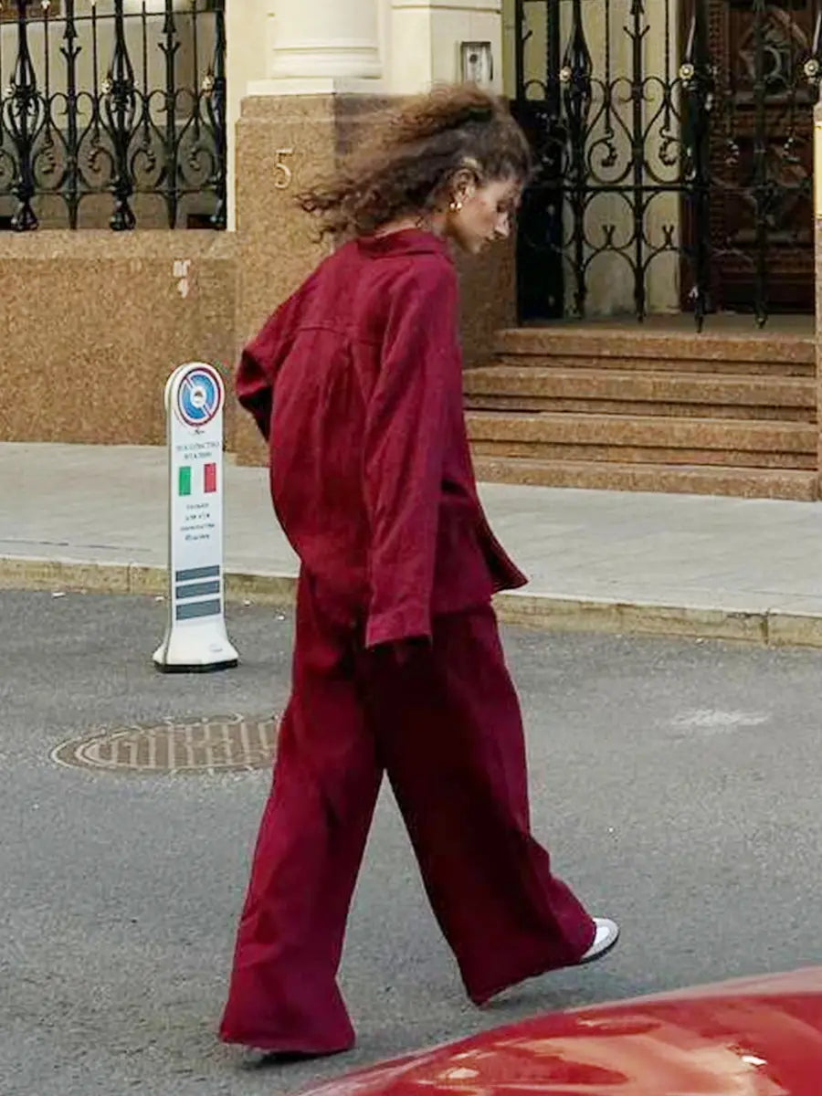 a woman wearing a deep red corduroy two-piece shirt trousers suit with wide-leg pants and a matching jacket featuring a long sleeve design