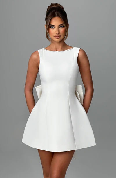 A sleek white backless sleeveless mini dress summer slim with a flared skirt and pearl embellishments along the neckline.