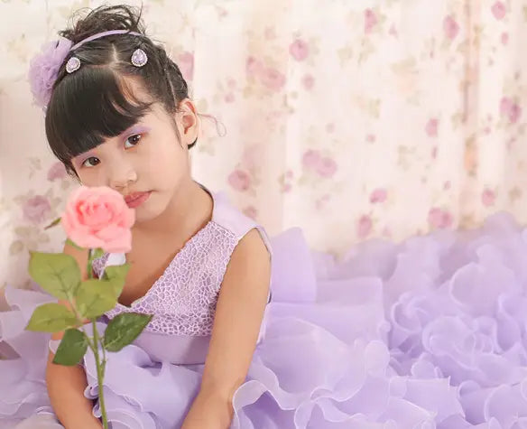 A young girl wearing a fuchsia layered ruffled lace dress flower girl tuxedo holding a pink rose.