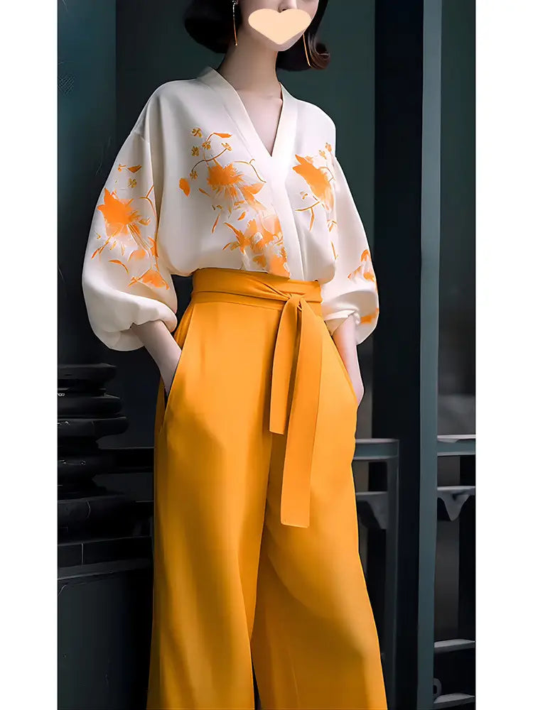 A flowing white silk blouse with orange floral embroidery and voluminous sleeves paired with high-waisted mustard yellow wide-leg pants in a slimming wear flab hiding shirt set.
