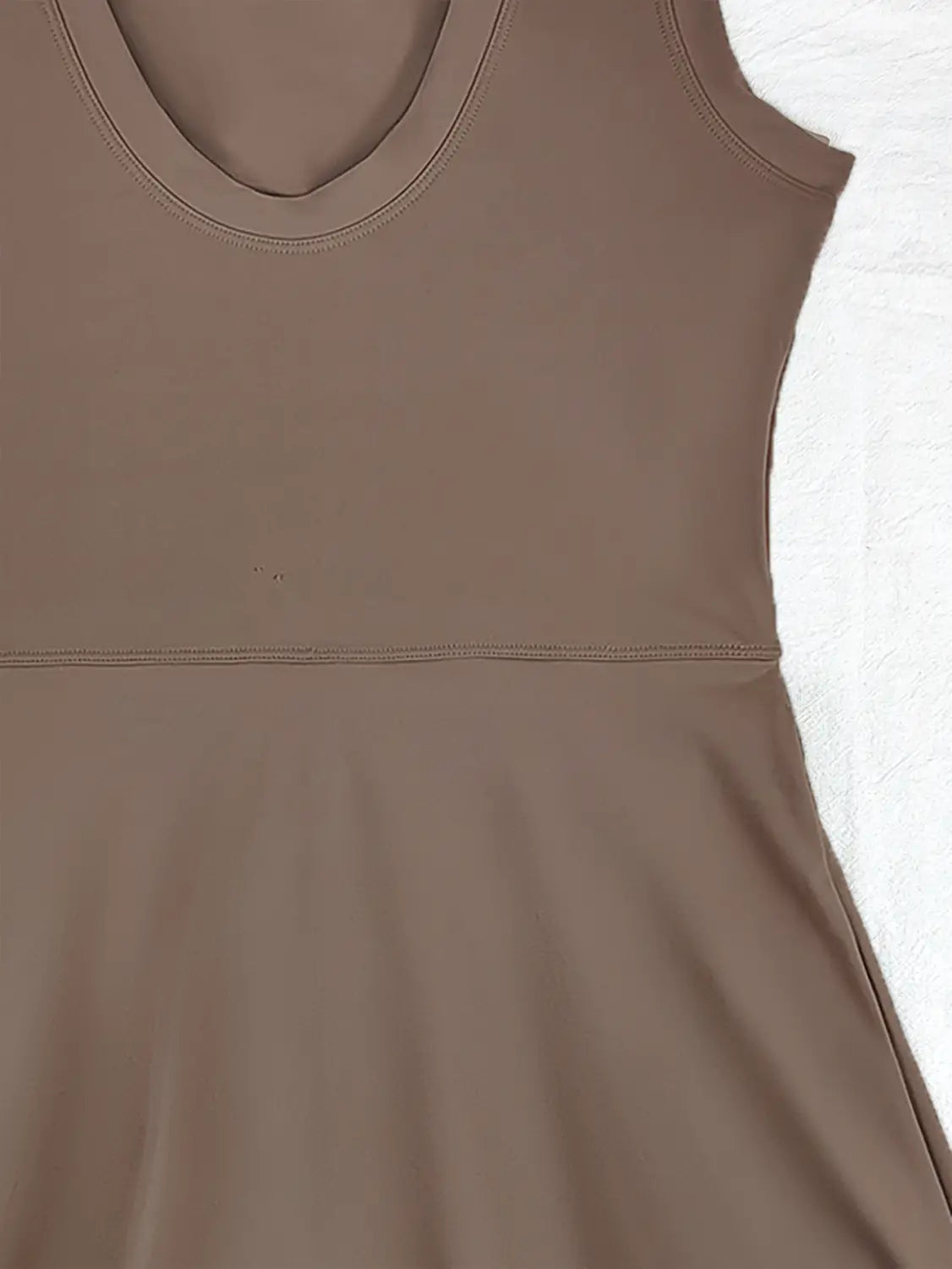 A taupe sleeveless skirt sport dress with a rounded neckline and smooth stretchy fabric designed as a yoga tennis skirt.