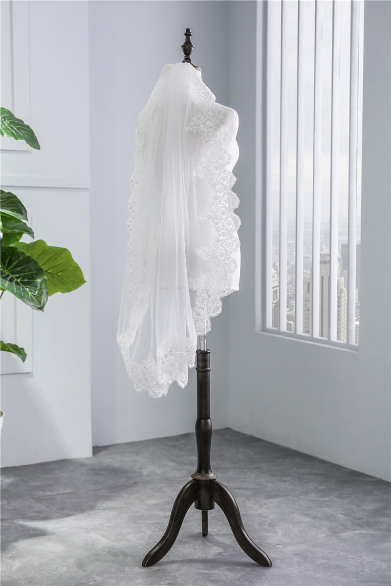 a delicate short veil soft mesh sequined lace in white ivory with intricate floral embroidery and scalloped edges displayed on a dark wooden mannequin stand