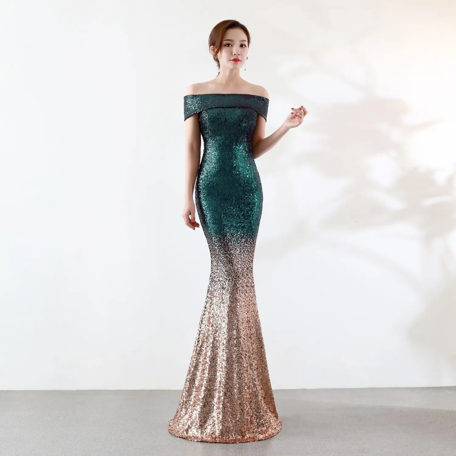 A shimmering mermaid-style birthday party dress with an off-the-shoulder neckline featuring a gradient of deep emerald green sequins transitioning to rose gold at the hem designed as a slimming dress slimming host gown.