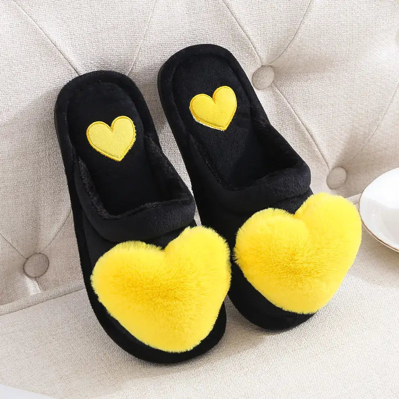 Black plush home slippers featuring bright yellow fuzzy heart decorations on the front and a matching embroidered heart on the insole designed as cute love slipper winter warm wear.