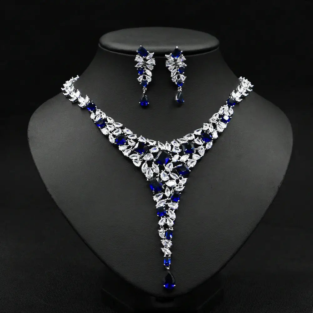 Elegant royal blue and clear crystal zircon necklace set featuring a v-shaped design with intricate leaf motifs and dangling teardrop accents in a colorful zircon necklace set.