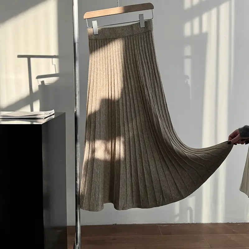 A beige ribbed knit pleated midi skirt with a korean elastic waist hanging on a wooden hanger.