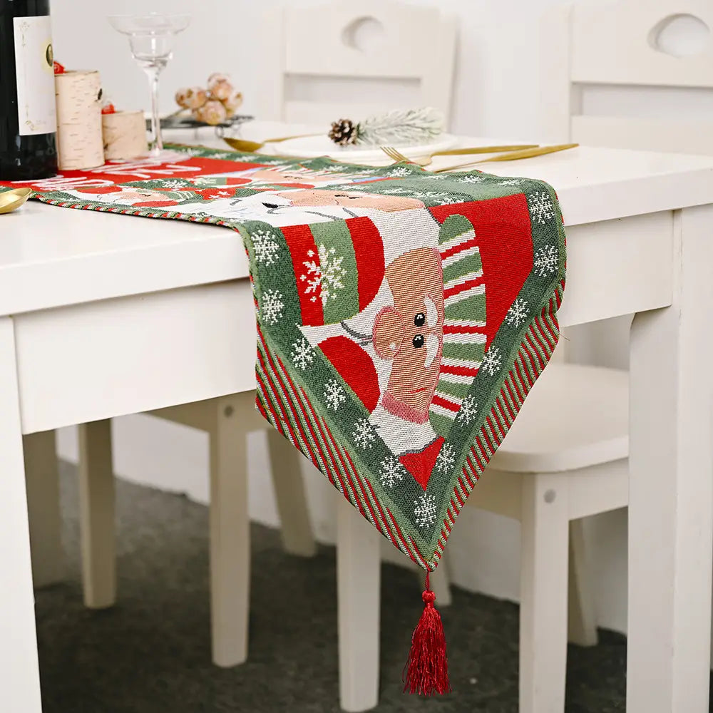 Woven christmas table runner in red and green featuring a central embroidered reindeer with snowflakes, striped patterns, and matching red tassels for festive christmas table decor.