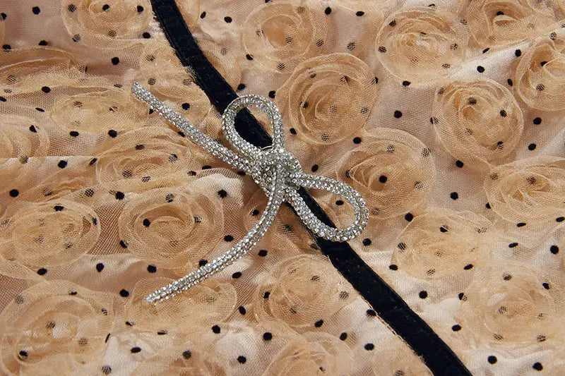 a sparkling silver bow brooch with clear crystals displayed on beige lace roses and black polka dots complements the blush pink lace slim drawstring dress.
