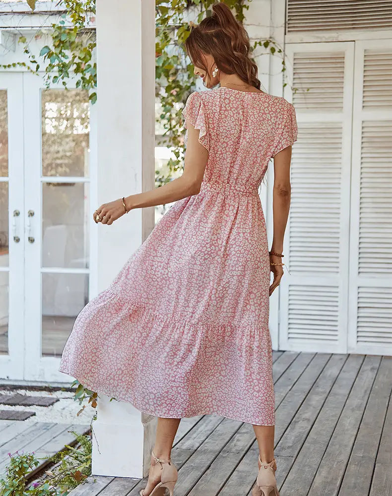 a flowing pink summer dress with a delicate white floral pattern featuring ruffle cap sleeves and a tiered skirt perfect for warm weather occasions