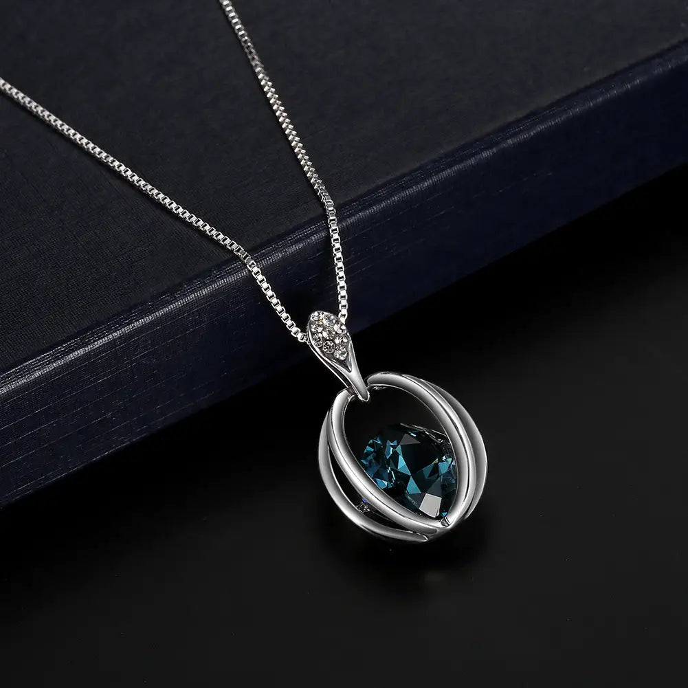 Silver pendant necklace with a deep blue faceted gemstone encased in an elegant intertwined metal design and sparkling accent stones at the bail, perfect as a crystal bridal necklace featuring fashion inlaid crystal details.