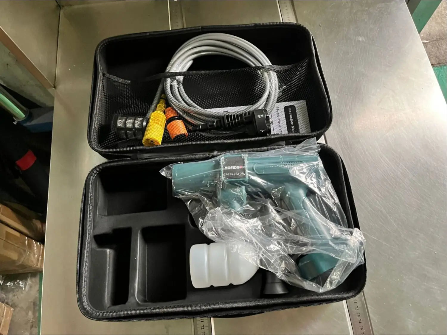 Teal multifunctional car wash high pressure water gun with white plastic container wrapped in clear plastic inside a black carrying case.