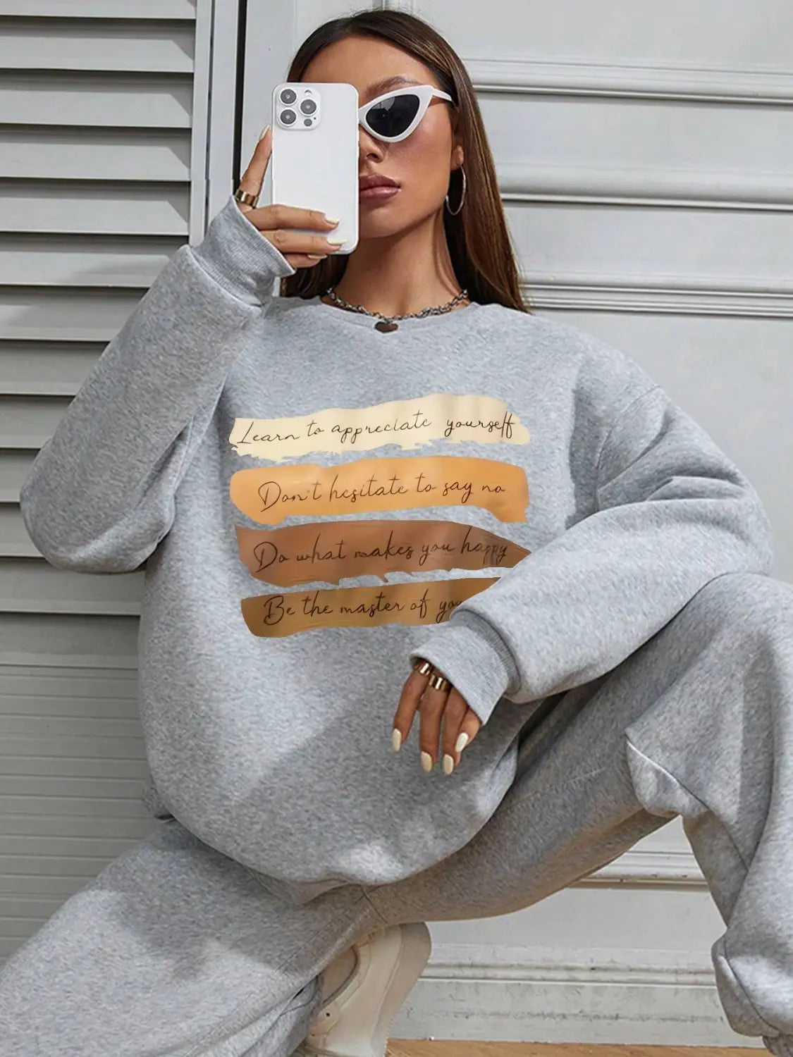 White oversized long sleeve sweatshirt in solid gray with beige and orange motivational phrases printed on the front for daily wear.