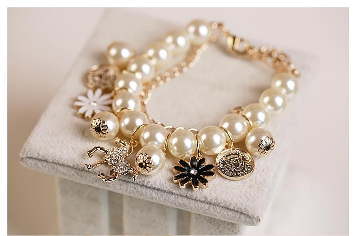 A delicate gold-toned pearl flower bracelet featuring cream-colored pearls, a black floral pendant, a rhinestone horse charm, and small coin-like accents.