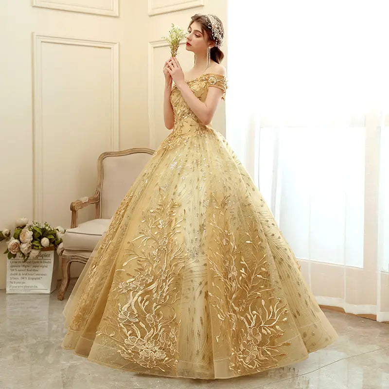 A shimmering gold off-the-shoulder solo performance costume tutu featuring intricate floral embroidery and a voluminous tulle skirt.