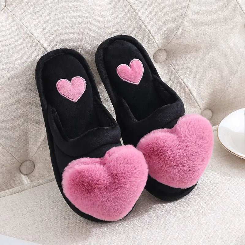 black fuzzy home slippers with pink heart-shaped pom-poms and embroidered hearts on the insole designed as cute love slippers for winter warm plush wear.