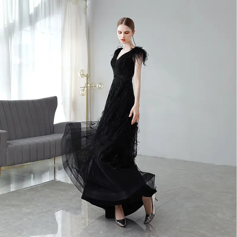 Elegant black double shoulder evening dress with sequins featuring feather detailing and a layered flowing skirt