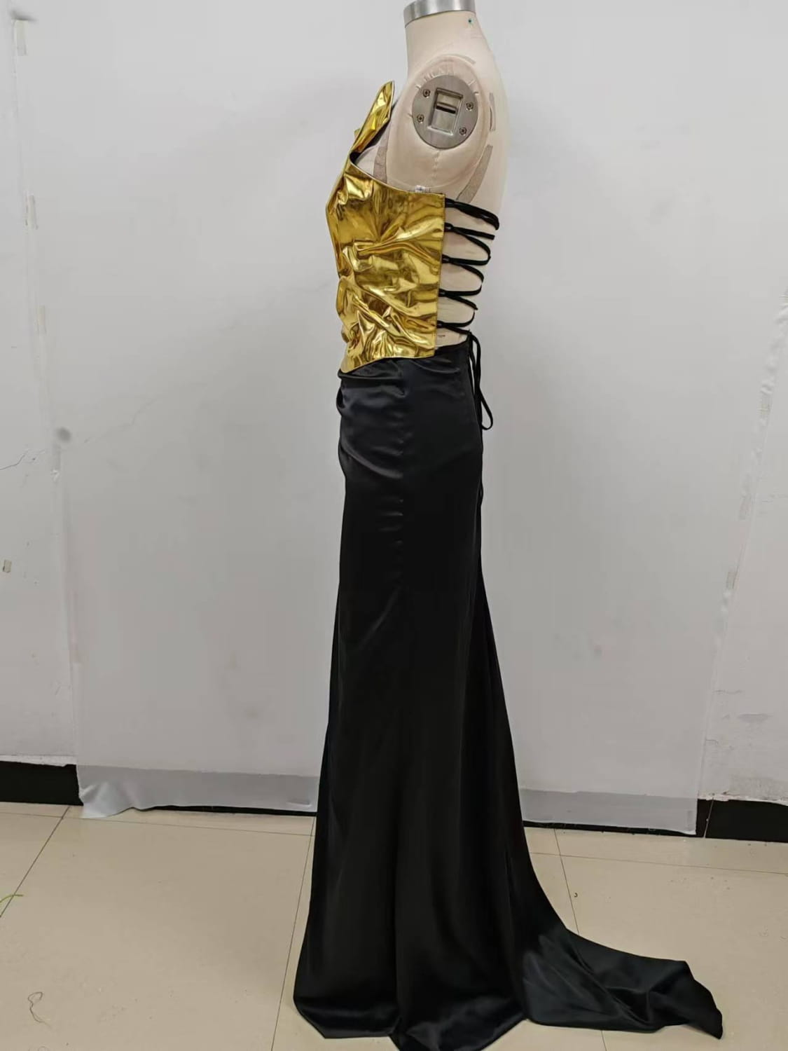 a shimmering gold metallic corset top with set sexy lacing paired with a sleek floor-length mop black dress featuring a one-shoulder slit mop black design
