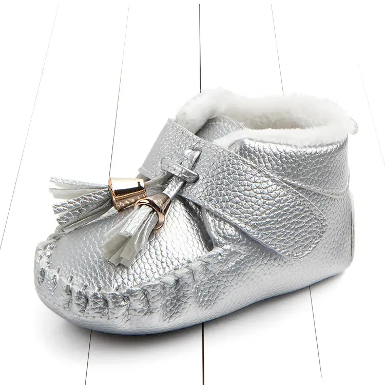 silver textured leather baby shoes with white faux fur lining and decorative tassel accent designed as non-slip toddler shoes