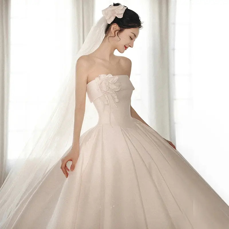 A flowing ivory satin strapless dress with an embroidered floral appliqué bodice and a voluminous big train skirt showcasing luxury women’s fashion.