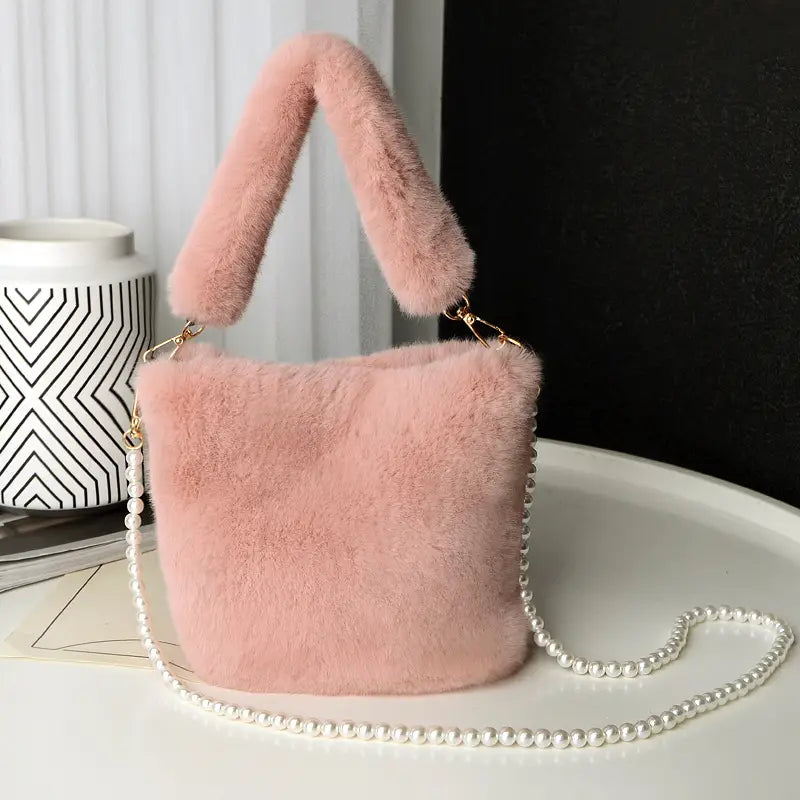 a soft pink plush bucket bag with a checkerboard plush bucket design featuring a fluffy handle and a delicate pearl chain design strap