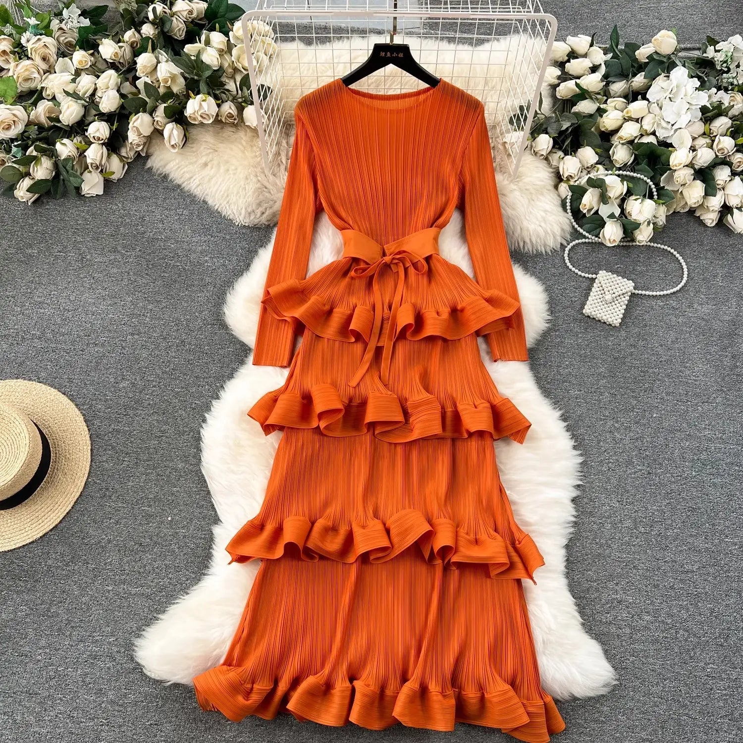 Vibrant orange pleated tiered dress with ruffled layers and a matching belt showcasing cake heavy industry pleated design.