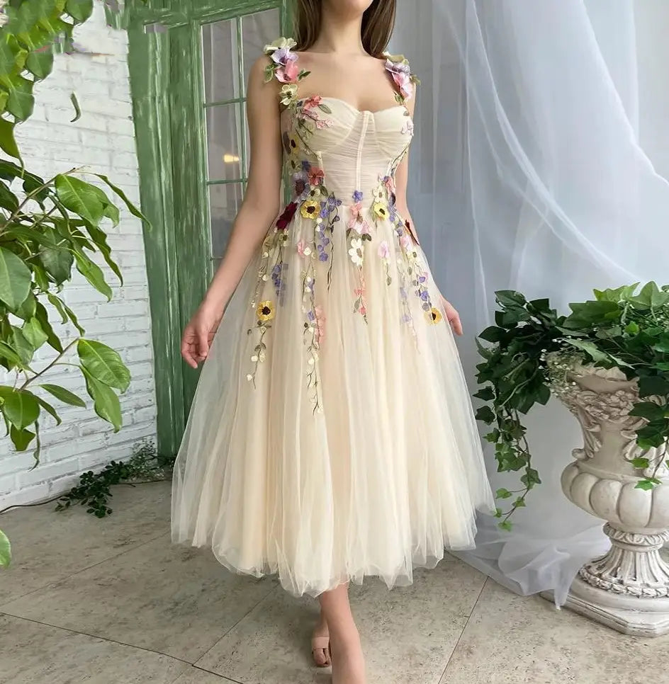 A delicate off-white light champagne tulle prom dress featuring intricate colorful floral embroidery cascading down the bodice and skirt.