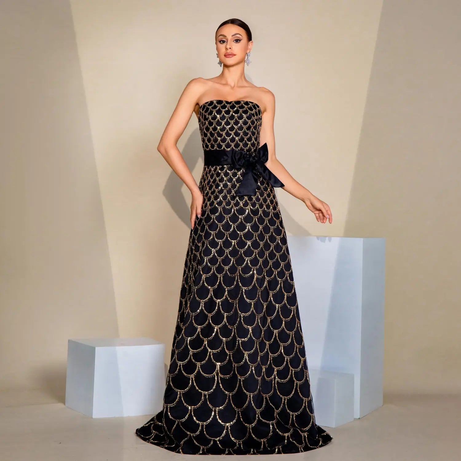 Black strapless large swing sequined evening dress featuring shimmering gold scale embroidery and a matching satin bow at the waist.