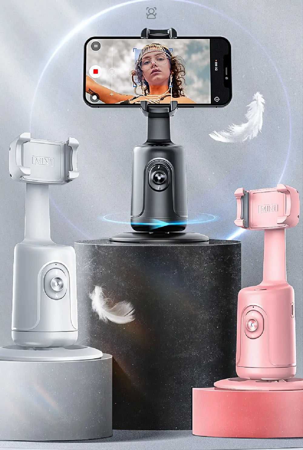 Three smartphone selfie stick phone holders in white, black, and pink with adjustable arms and camera mounts featuring face tracking gimbal technology.