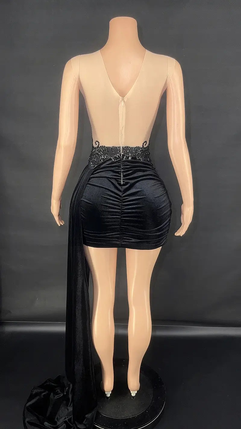 black velvet luxury evening dress female showing the back side with a ruched mini skirt, embellished waistband, and a flowing side train for summer luxury evening wear.