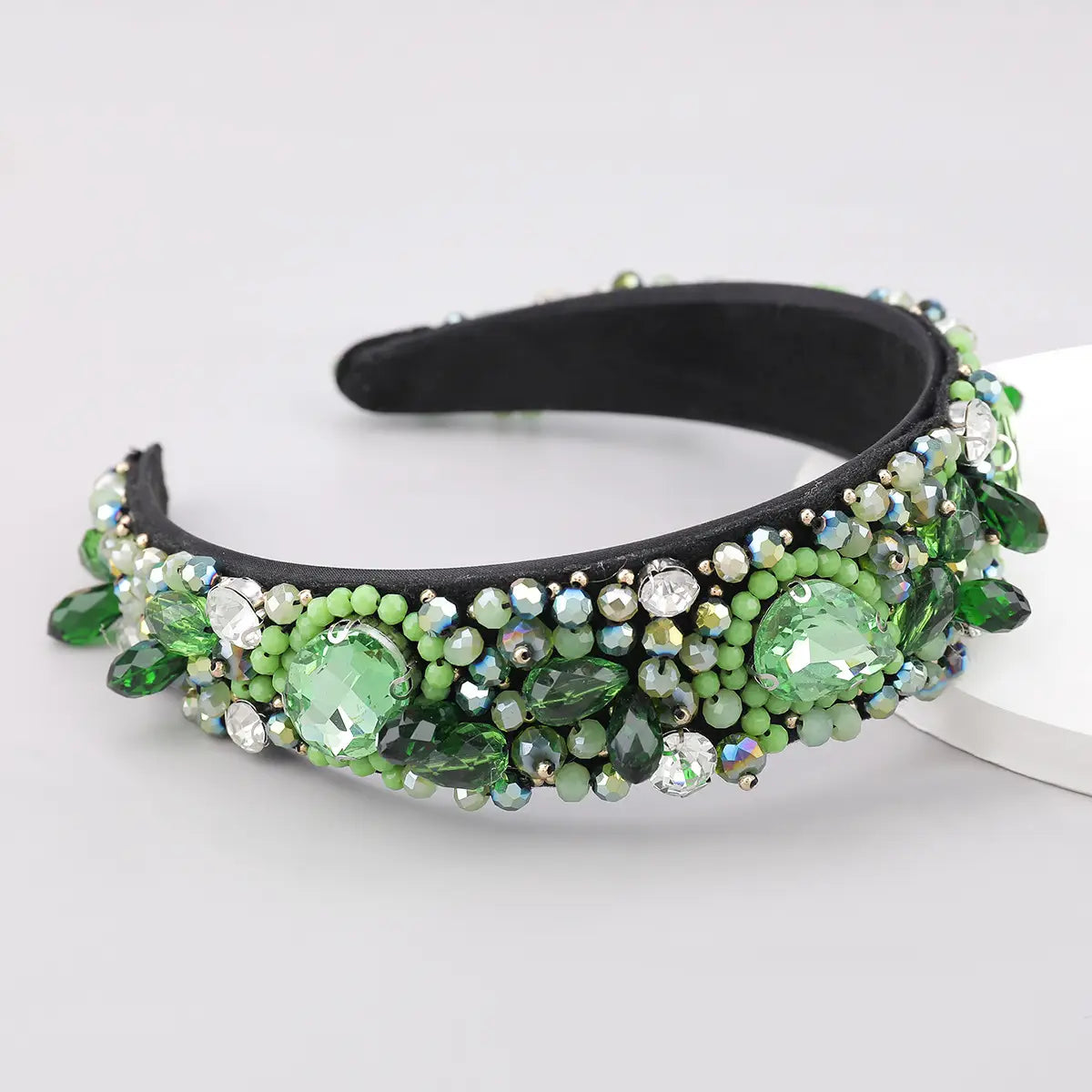 A black headband adorned with an intricate array of green and clear crystal geometric glass rhinestones and beads.