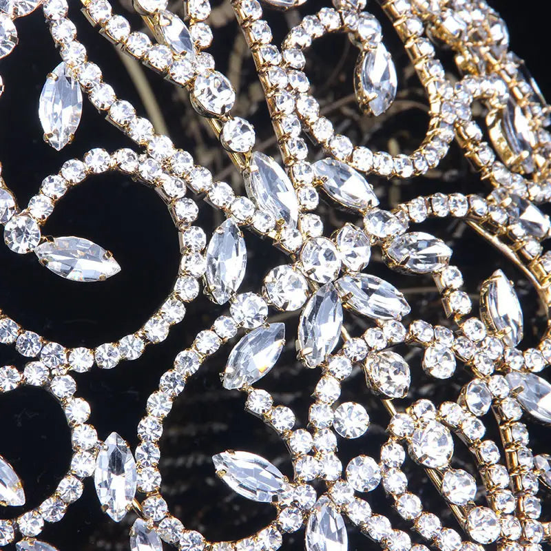 A sparkling gold-toned luxury rhinestone bridal crown featuring intricate patterns of clear marquise and round crystals with a starburst accent.