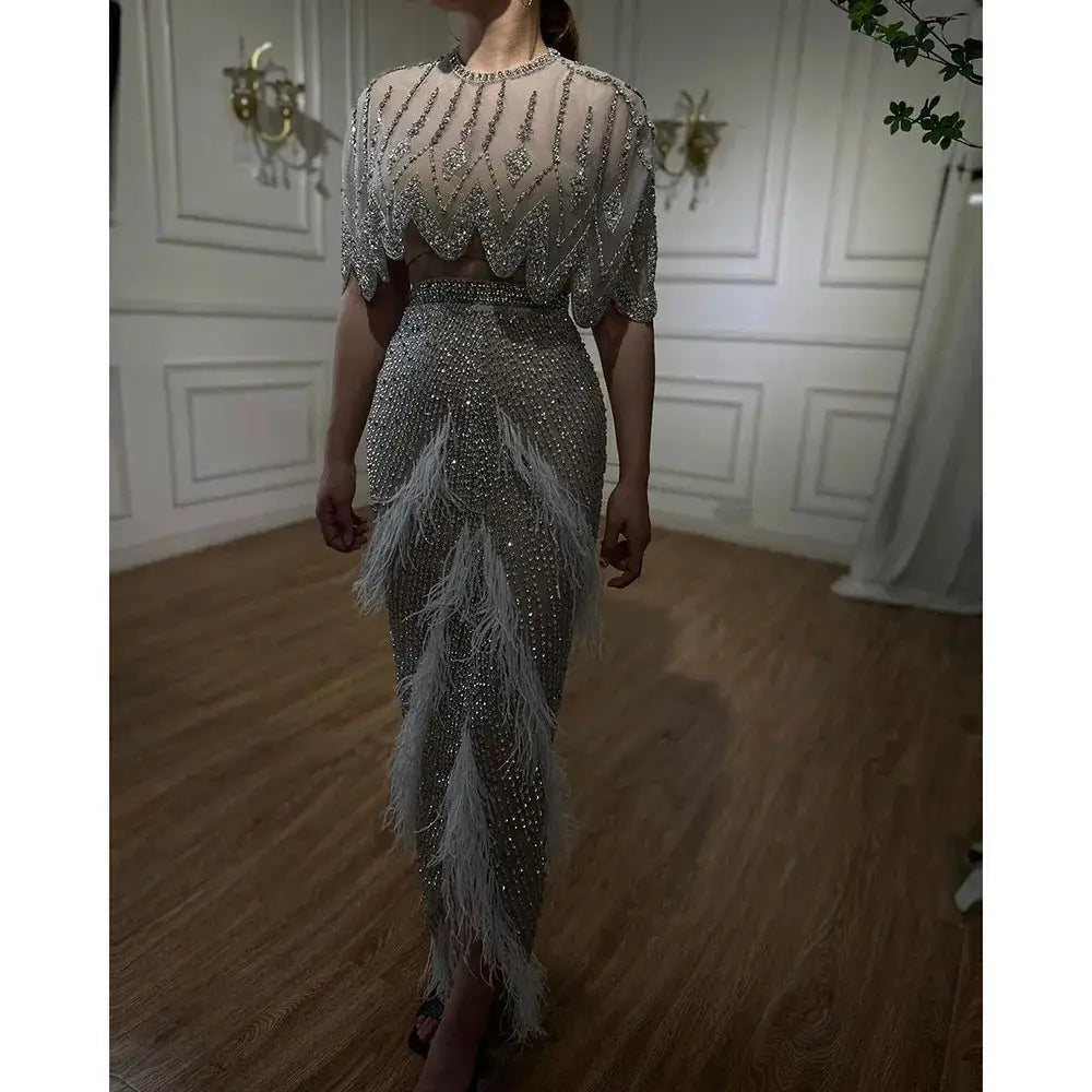 A silver nude evening dress featuring a shimmering silver beaded gown with feather accents and a sheer embellished bodice ideal for formal occasions.