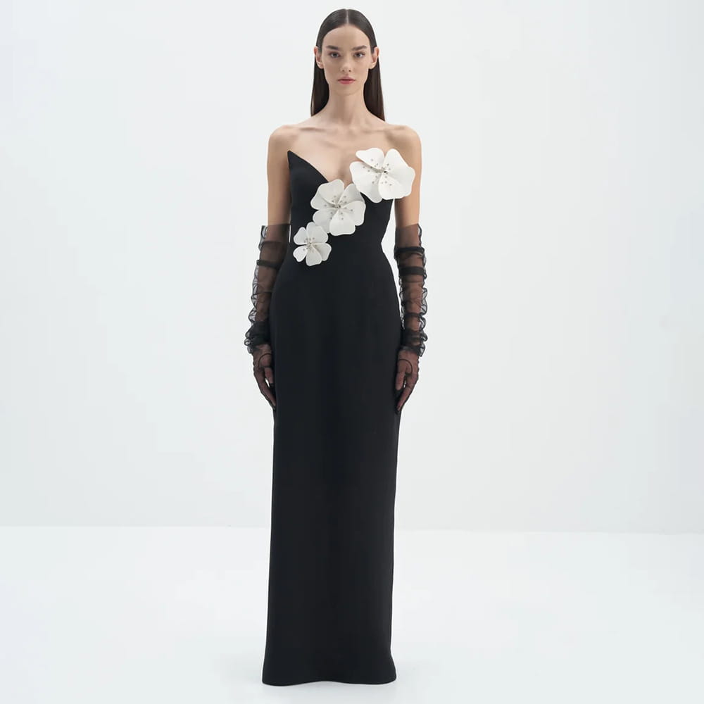 Elegant black backless bandage gown featuring a strapless bandage chest adorned with large white floral appliqués and sheer lace gloves.
