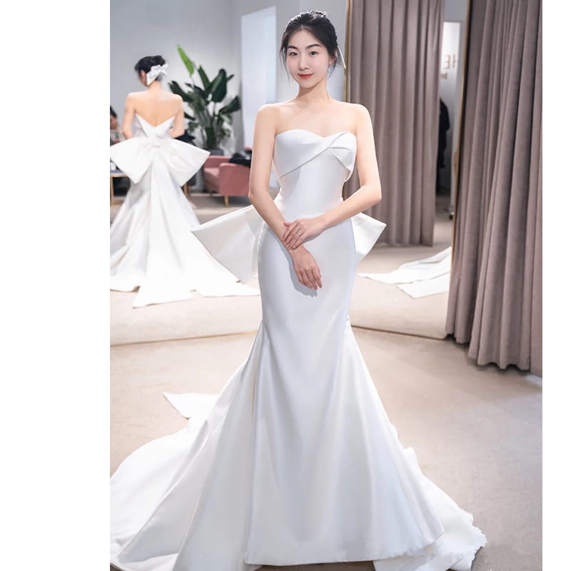 A sleek white satin small trailing temperament wedding dress in mermaid style with a strapless sweetheart neckline and dramatic ruffled accents at the waist.