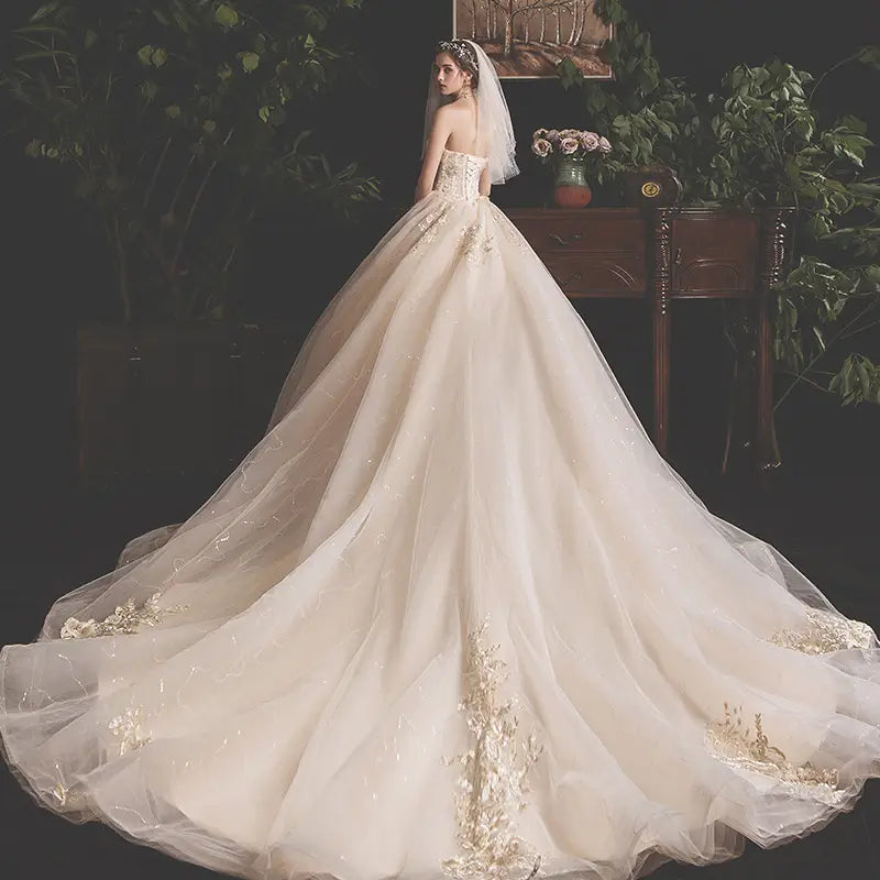 champagne lace wedding gown for pregnant woman in flowing ivory polyester fiber with delicate gold floral embroidery on the bodice and train, featuring a strapless design and sheer veil, main fabric suitable for maternity wear.