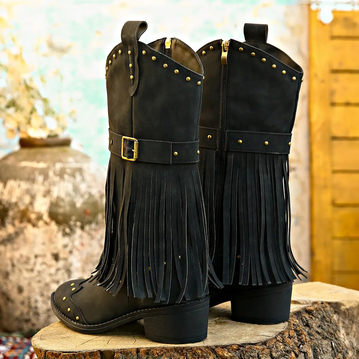 Black suede cowboy boots in retro winter fashion with gold-tone studs, matching belt buckle, fringe detailing, and a fashion square heel.