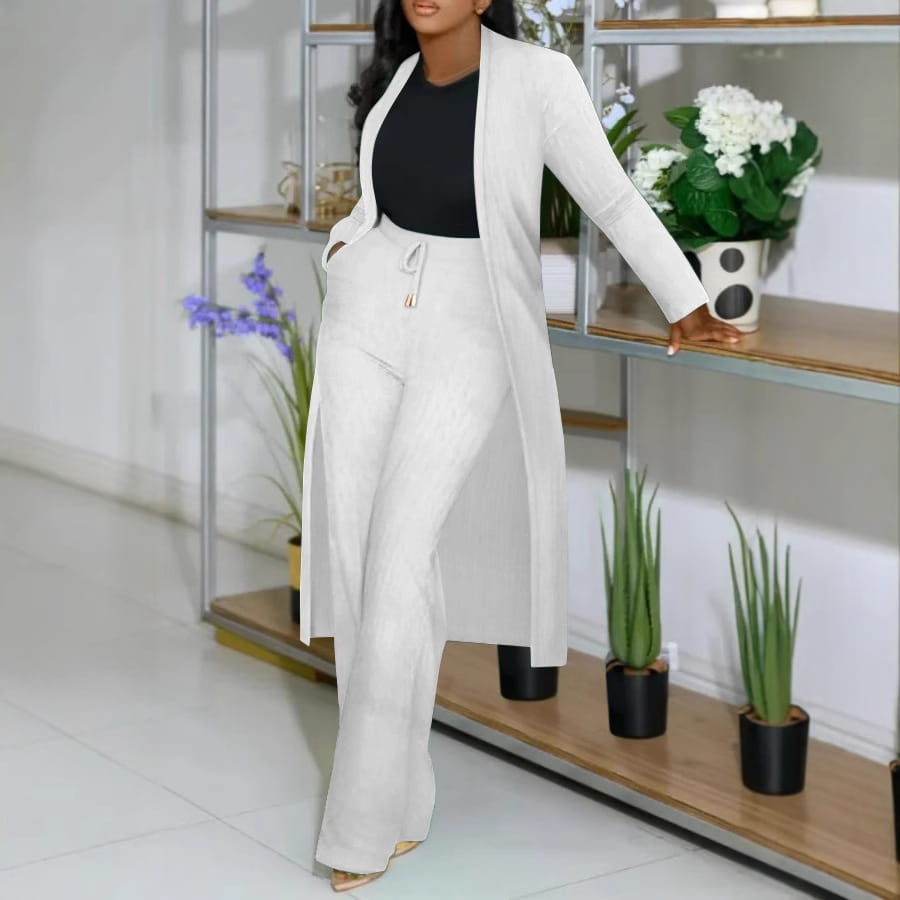 A woman wears a white long cardigan sunken stripe set featuring a blazer with wide sleeves and matching sunken stripe wide leg pants paired with a black top.