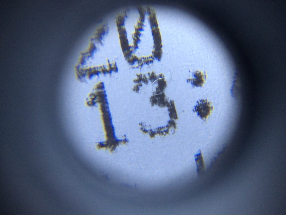 a close-up view through the eyepiece of a digital microscope camera with led light focusing on handwritten dark ink markings on a light-colored surface.