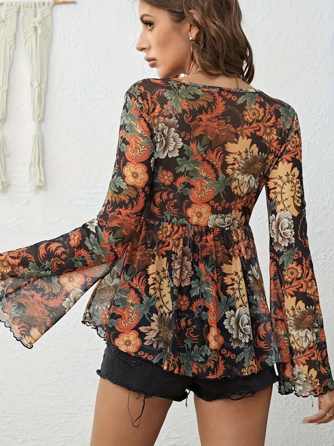 A black sheer mesh printed blouse with a vibrant orange red and green floral pattern featuring long knotted flare sleeves and a peplum waist.