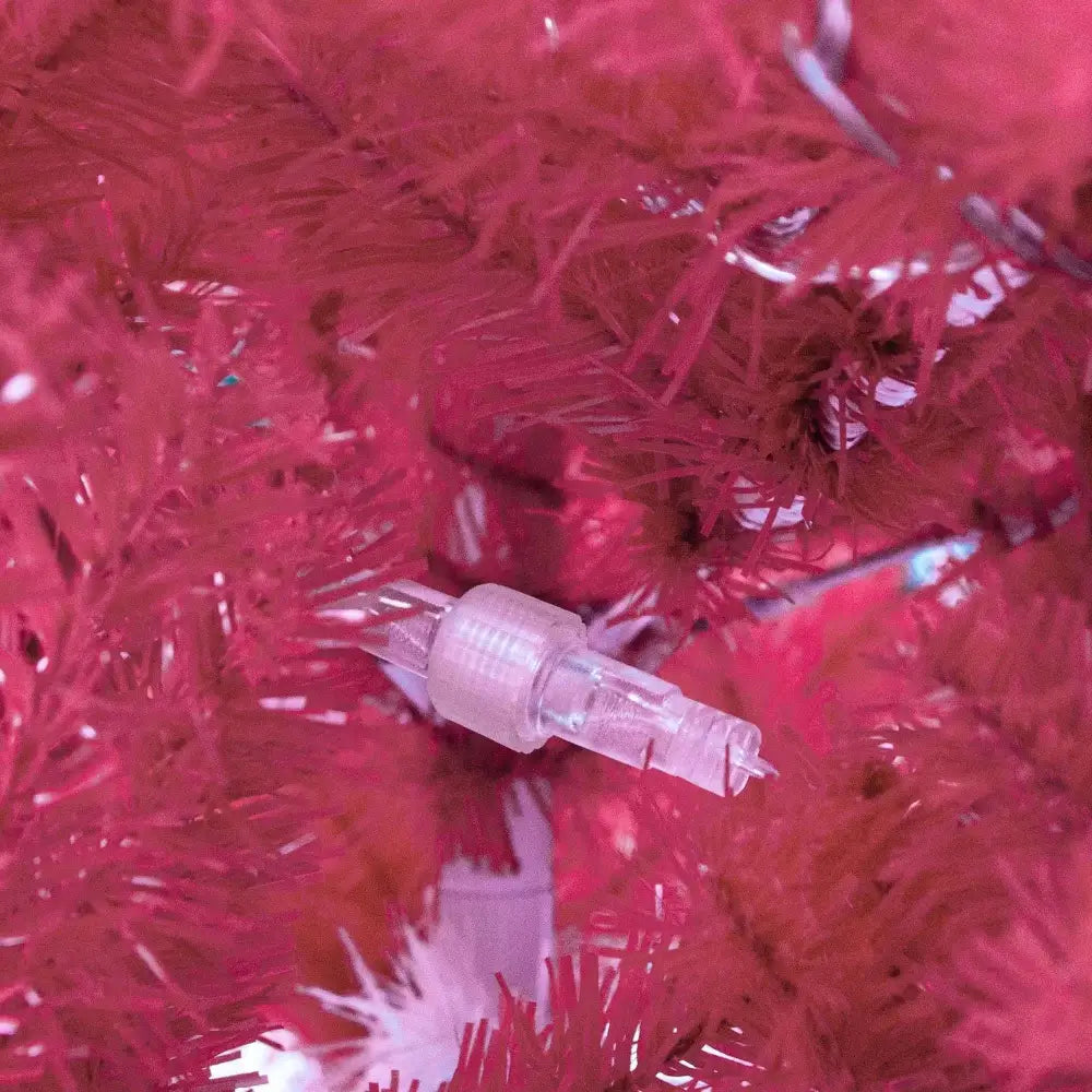 A clear plastic christmas light bulb nestled in vibrant red artificial branches on a 6 foot articulated fir tree with led lights