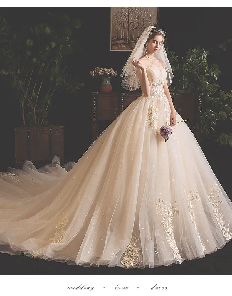 A flowing ivory bride summer tube gown in mori style with intricate gold lace detailing and a voluminous tulle style trailing skirt.