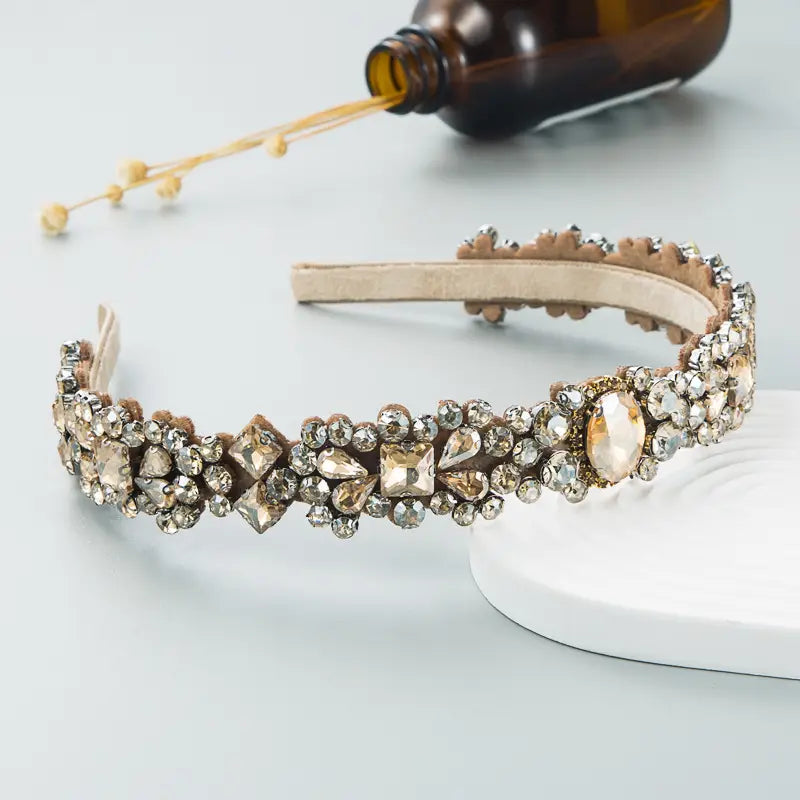 A delicate beige court style headband featuring an intricate array of clear and champagne-colored crystals set on a soft fabric base, inspired by baroque vintage court design.